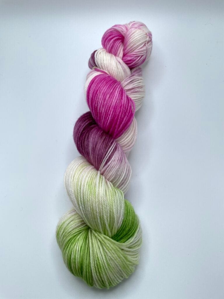A skein of Loch Briar Knits yarn with a gradient of colors including green, white, pink, and purple, neatly twisted together against a plain white background.