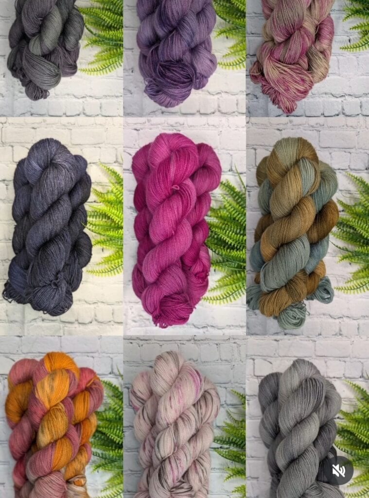 A collage of nine colorful yarn bundles displayed against a white brick wall with green ferns in the background, showcasing the vibrant hues from Yarn Divas. The yarns are in various shades including dark gray, purple, maroon, dark blue, bright pink, olive green, orange, peach, and light gray.