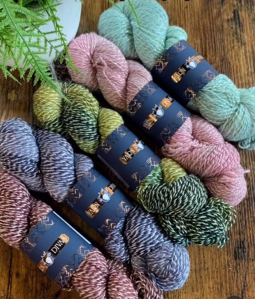 Five skeins of variegated yarn in pastel colors from Dye Studio, each wrapped with a label that reads 
