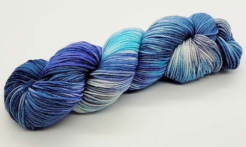 A skein of multicolored yarn with shades of blue, turquoise, and gray, coiled neatly against a white background, ready for creative needles to bring it to life.
