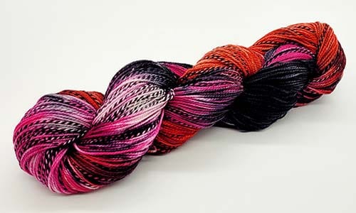 A hank of multicolored yarn with interwoven shades of pink, black, red, and white, neatly twisted and placed against a plain white background awaits the magic of needles.