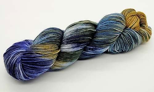 A skein of multicolored yarn featuring shades of blue, green, gray, and gold, arranged in a twisted hank on a plain white background. The yarn has a smooth and plush texture, perfect for knitting or crocheting projects with your favorite needles.