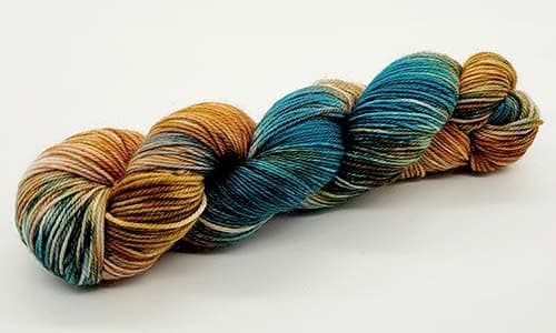 A skein of multi-colored yarn with shades of teal, brown, and gold lies against a plain white background. The yarn is tightly wound, perfect for creative nerds ready to wield their needles and showcase its vibrant hues.