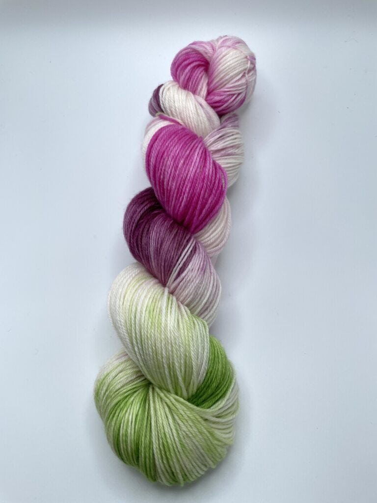 A skein of Loch Briar Knits yarn with a gradient of colors including green, white, pink, and purple, neatly twisted together against a plain white background.